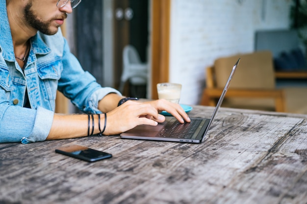 young attractive business man in a cafe works for a laptop, drinks coffee.