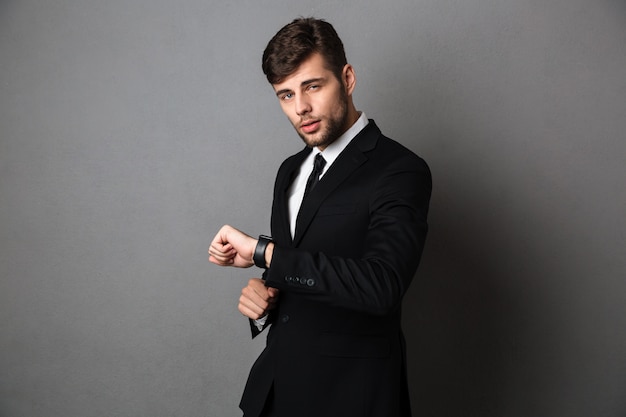 Young attractive businessman in formal wear checking time on his wristwatch, 