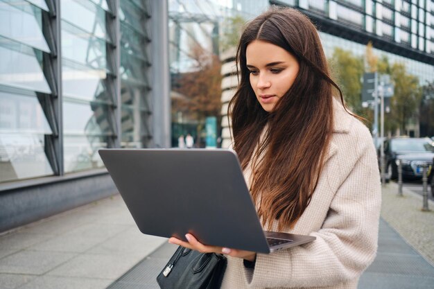 Young attractive businesswoman intently working on laptop on city street