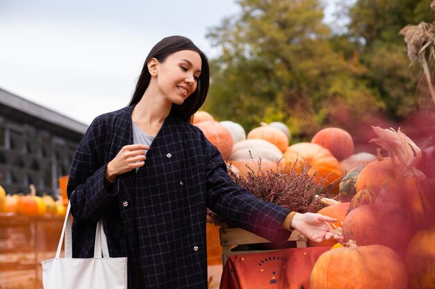 屋外のハロウィーンの日のカボチャを喜んで探している農家の店で若い魅力的なカジュアルな女性