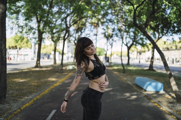 Молодая привлекательная кавказская женщина с татуировками стоит в парке и делает милое лицо
