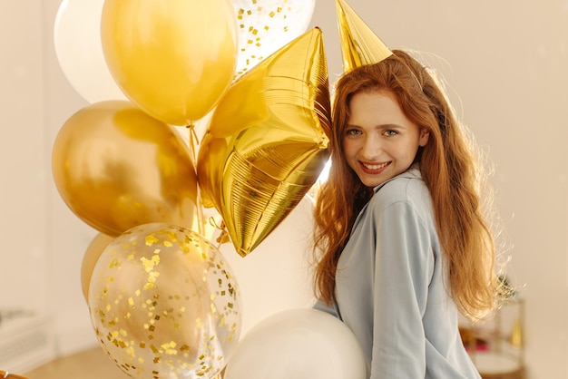 Young attractive caucasian girl with long red hair wearing pajamas holding balloons posing for camera Bachelorette party concept