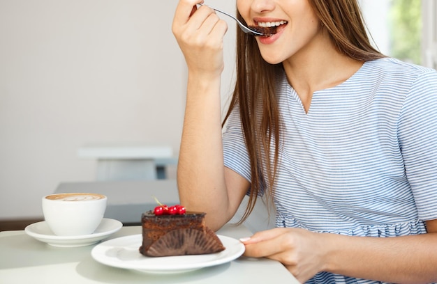 若い魅力的な白人女性は正午にモダンなコーヒーショップでホットコーヒーとチョコレートケーキを食べることをお楽しみください