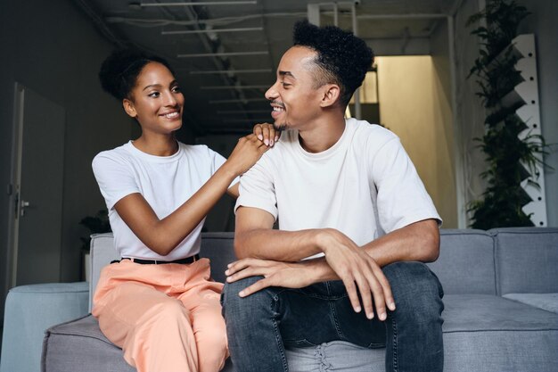 젊고 매력적인 쾌활한 캐주얼 아프리카계 미국인 부부는 현대 가정의 소파에서 행복하게 서로를 바라보고 있습니다