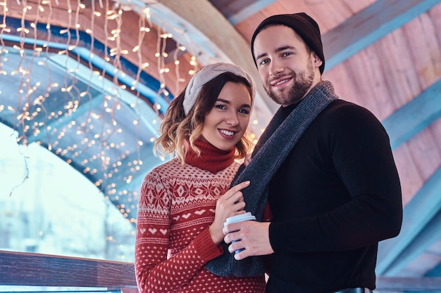 Young attractive couple on a date in an ice skating rink, standing in the hall and drinking coffee