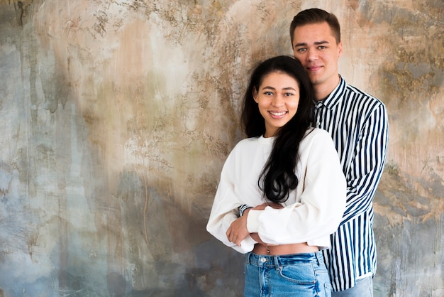 Young attractive couple hugging against concrete wall