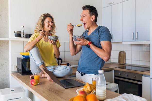 Young attractive couple of man and woman eating breakfast together in morning at kitchen