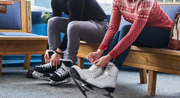 Young attractive couple sitting on a bench and tying shoelaces of ice hockey skates in the locker room