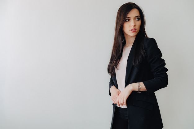 Молодая привлекательная эмоциональная девушка в деловом стиле одежды на простом белом фоне в офисе или аудитории