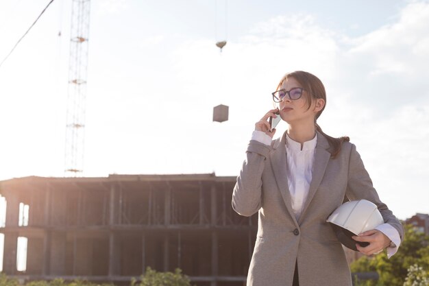 Молодой привлекательный женский архитектор говоря на мобильном телефоне на строительной площадке