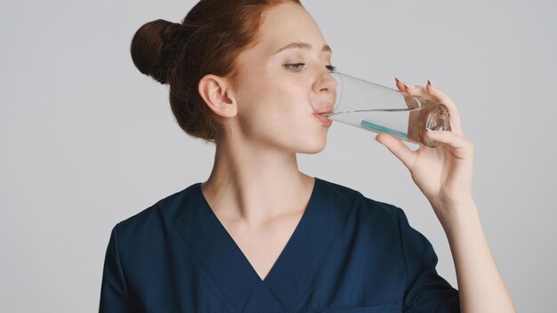 白い背景の上のカメラで水を飲む若い魅力的な女性医師