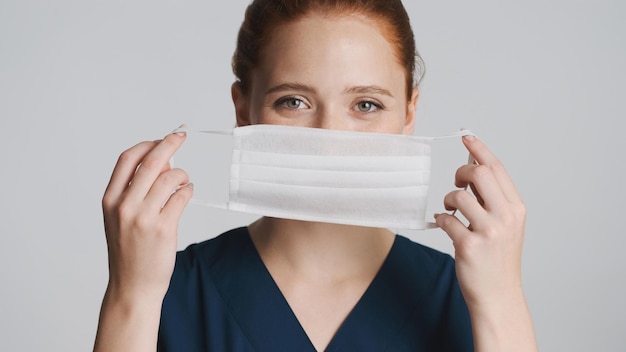흰색 배경 안전 개념 위에 카메라에 의료 마스크를 쓴 젊은 매력적인 여성 의사