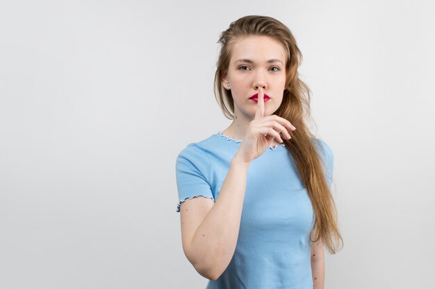 Young attractive girl in blue shirt and beautiful hair showing silence sign