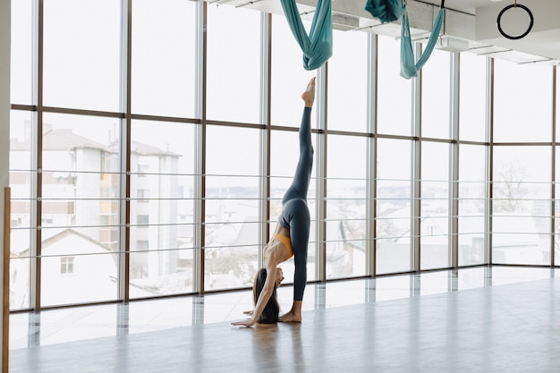 La giovane ragazza attraente che fa la forma fisica si esercita con yoga sul pavimento contro la superficie delle finestre panoramiche