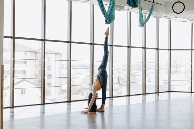 Young attractive girl doing fitness exercises with yoga on the floor against the surface of panoramic windows