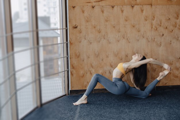 Young attractive girl doing fitness exercises with yoga on the floor on a wooden background