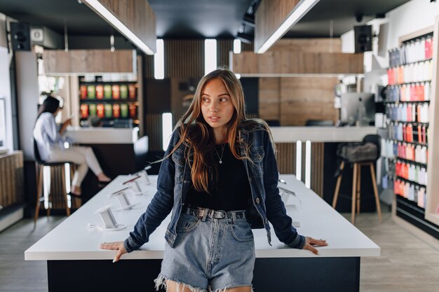 Young attractive girl in electronics store standing at table.