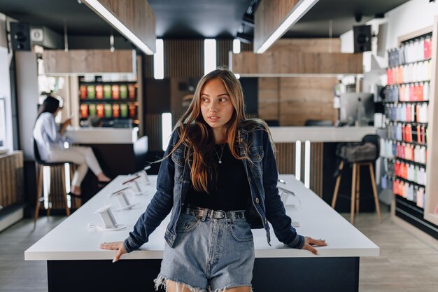Молодая привлекательная девушка в магазине электроники стоя на таблице.
