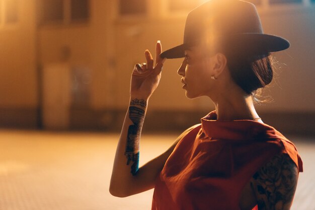 The young, attractive girl in a hat poses to the camera at night