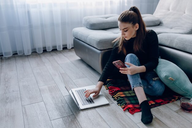 Young attractive girl at home working with a laptop and talking on the phone. comfort and coziness while at home. home office and work from home. remote online employment.