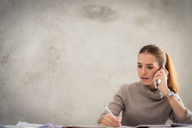 Young attractive girl talking on mobile phone and smiling while sitting alone in coffee shop during free time and working on tablet computer. Happy female having rest in cafe. Lifestyle