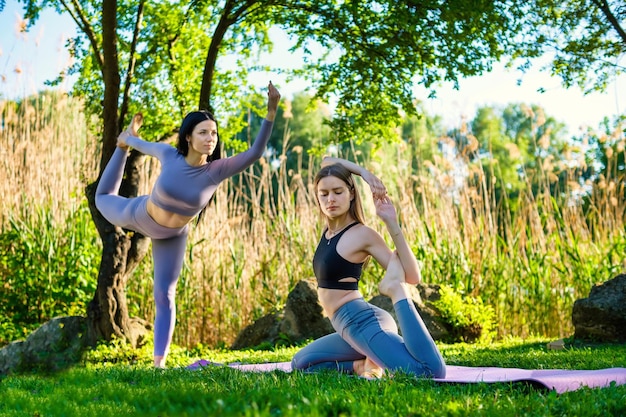 Young attractive girls practicing different yoga streches in the green park near blooming trees