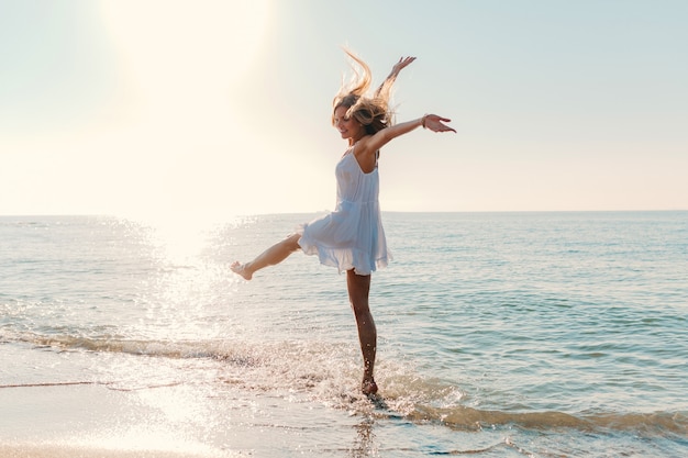 Молодая привлекательная счастливая женщина танцует, оборачиваясь на берегу моря в солнечном летнем стиле моды