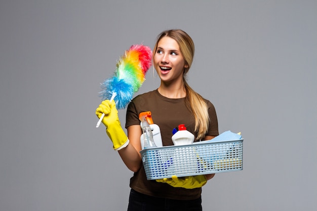 Young attractive housewife wearing casual clothes, latex gloves holding full basin of cleaning agent isolated on white