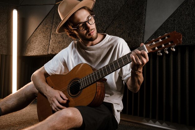 젊은 매력적인 남성 음악가는 녹음실에서 신중하게 기타를 연주합니다. 스튜디오에서 노래를 작곡하는 잘생긴 세련된 남자