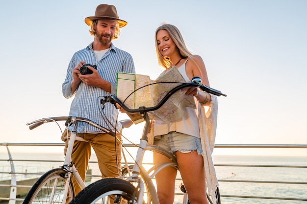 無料写真 地図を持って自転車で旅行する若い魅力的な男性と女性、流行に敏感なスタイルの衣装、一緒に楽しんでいる友人、カメラで写真を撮る観光