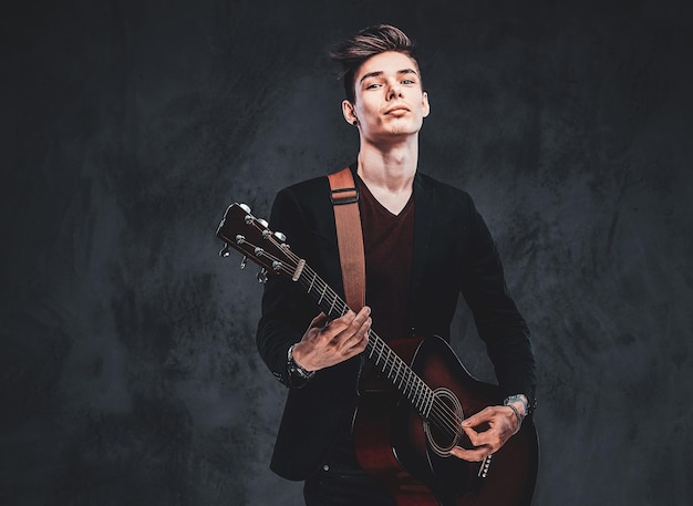 젊은 매력적인 남자가 사진사를 위해 포즈를 취하는 동안 스튜디오에서 어쿠스틱 기타를 연주하고 있습니다.