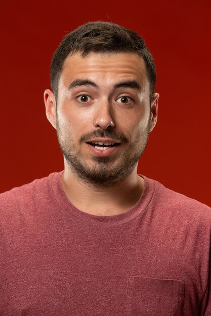 The young attractive man looking suprised isolated on red