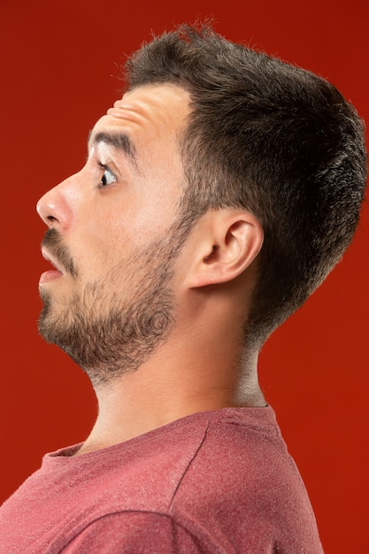 The young attractive man looking suprised isolated on red