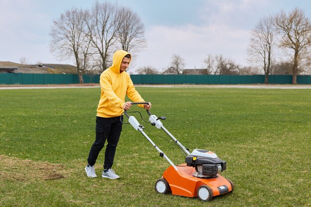 Young attractive man trimming grass with cutter