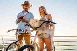 Free photo young attractive man and woman traveling on bicycles holding map, hipster style outfit, friends having fun together, sightseeing taking photo on camera