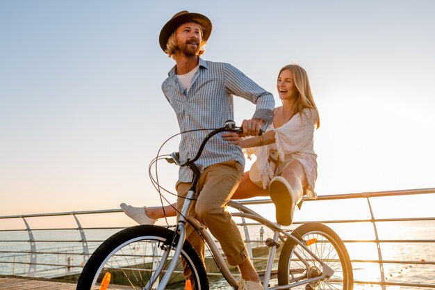 自転車で旅行する若い魅力的な男性と女性、日没の海のそばの夏休みのロマンチックなカップル、自由奔放に生きるヒップスタースタイルの衣装、一緒に楽しんでいる友達