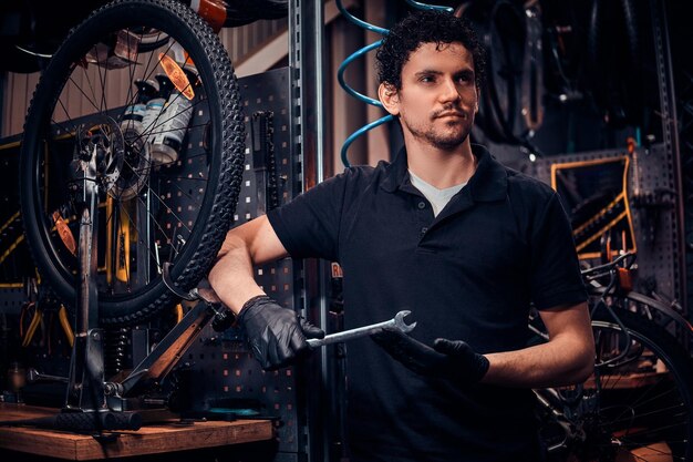 Young attractive mechanic is posing next to bicycle at his own workshop.