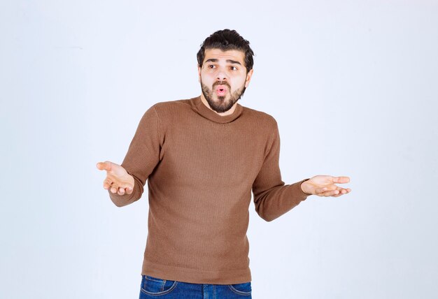 young attractive model in brown sweater posing on white wall.