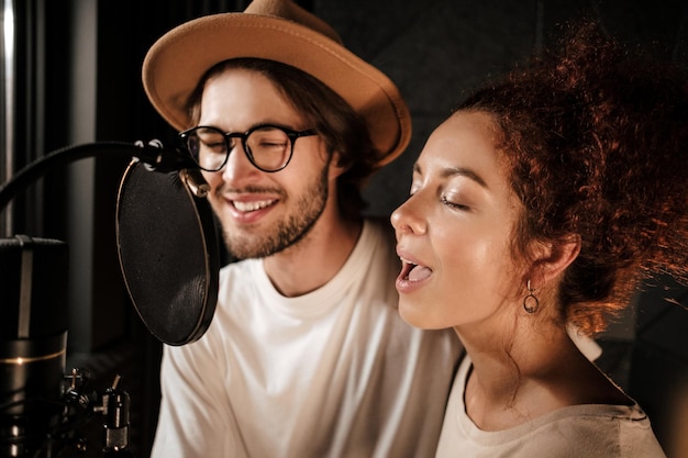 Young attractive musicians sensually singing working together on new music album in modern sound recording studio