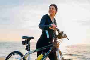 Free photo young attractive slim woman riding bicycle, sport in morning sunrise summer beach in sports fitness wear, active healthy lifestyle, smiling happy having fun