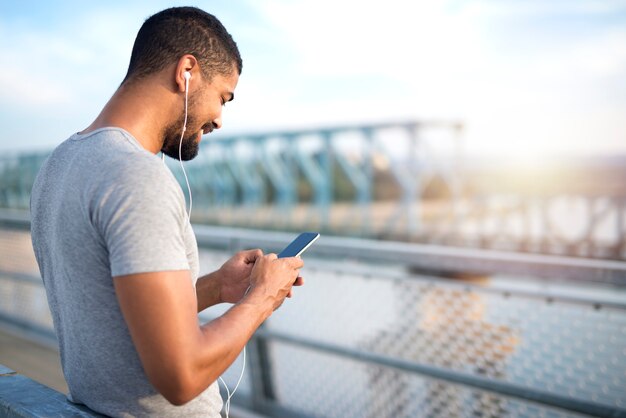 電話を使用して橋の上で笑顔の若い魅力的なスポーティな男