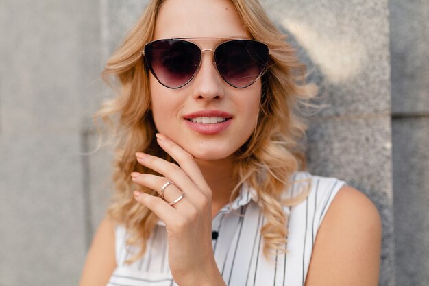 Young attractive stylish blonde woman walking in city street in summer fashion style dress wearing sunglasses