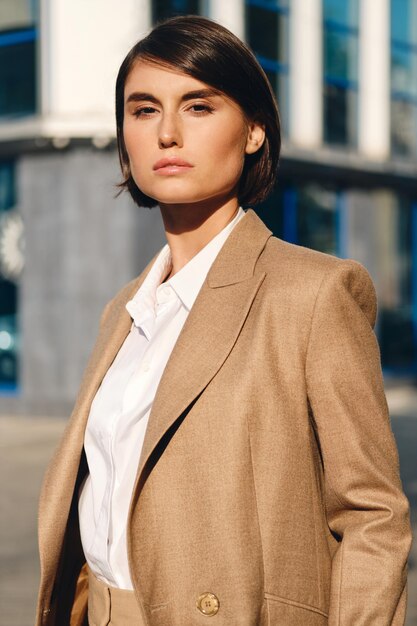 Young attractive stylish businesswoman in suit intently looking in camera on city street