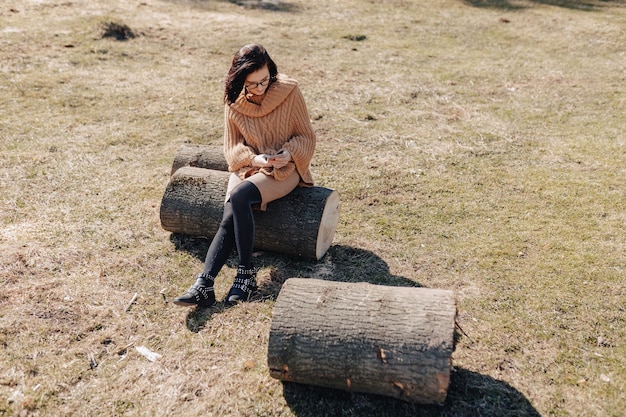 Молодая привлекательная стильная девушка на природе на фоне леса с телефоном в солнечный день