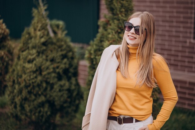 Young attractive woman in beige coat by the bushes