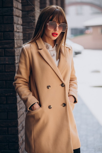 Молодая привлекательная женщина в бежевом пальто позирует на улице