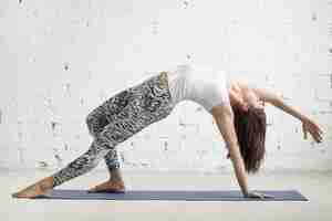 Free photo young attractive woman in camatkarasana pose, white studio backg