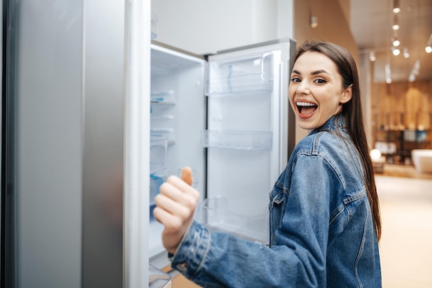 Молодая привлекательная женщина, выбирая холодильник в гипермаркете