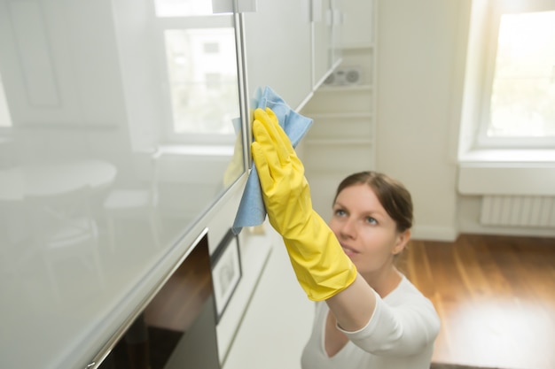 Young attractive woman cleaning an upper surface of kitchen clos