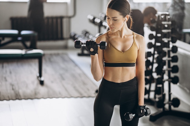 Young attractive woman exercising with dumbbells at the gym